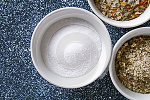 Different types of salt in glass bowls on a dark gray table.