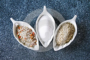 Different types of salt in glass bowls on a dark gray table.