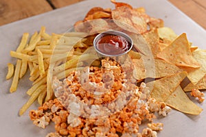 Different types of salty snacks for beer with tomato sauce. French fries, potato chips, nachos tortilla chips, popcorn.