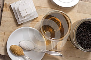 Different types of sugar lie on a wooden board. Tea brewed in a glass.