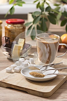 Different types of sugars and sweets lie on a wooden counter. Honey, loose white sugar and cane sugar lie on teaspoons in a white