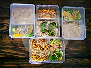 Different types of takeaway food in microwavable containers on a wooden background.