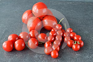 Different types of tomatoes on branches with rosemary and sea salt on a dark grey abstract background. Healthy eating