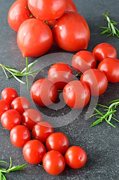 Different types of tomatoes on branches with rosemary and sea salt on a dark grey abstract background. Healthy eating