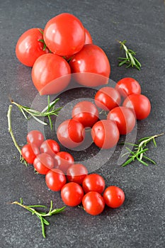 Different types of tomatoes on branches with rosemary and sea salt on a dark grey abstract background. Healthy eating