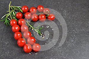 Different types of tomatoes on branches with rosemary and sea salt on a dark grey abstract background. Space for text