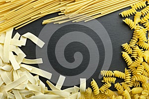 Different types of uncooked dried pasta on the black surface.Free space for text