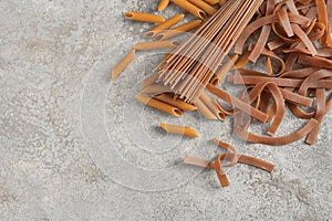 Different types of wholegrain pasta, tagliatelle, and penne rigate, on a rustic gray stone background, healthy noodle alternative