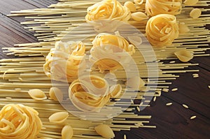 Different types of yellow raw pasta on wooden background