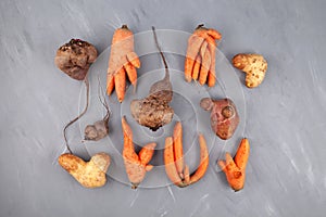 Different Ugly vegetables potato; carrot; beetroot on grey textured background, top view. Concept - Using in cooking imperfect