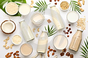 Different vegan milks and ingredients on white background, flat lay