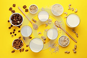 Different vegan milks and ingredients on yellow background, flat lay