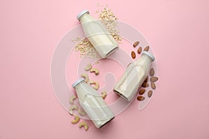 Different vegan milks, oat flakes and nuts on pink background, flat lay