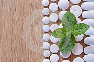 Different white pills and foliage mint on a wooden background