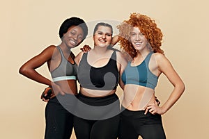 Different Women. Group Of Diversity Models Portrait. Smiling Multicultural Female In Fitness Clothes Posing On Beige Background.