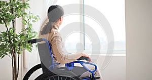 Differently abled woman in wheelchair looking out through window