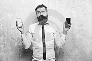 Difficult choice. hipster or bearded man compare mobile phone and smartphone