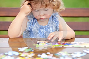 Difficult task. Tired child playing jigsaw with serious face.