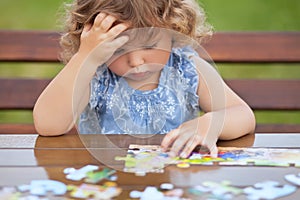 Difficult task. Tired child playing jigsaw with serious face.