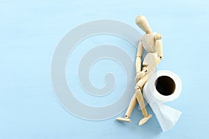 digestion or constipation health problen. Wooden figure sit on a roll of toilet paper. blue background