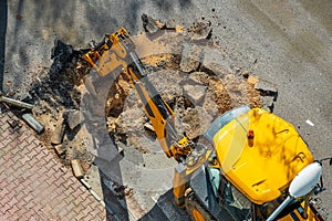 Digger digging asphalt to repair a water fault in a street