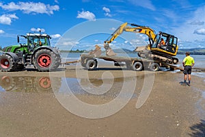 Digger on trailer behind tractor on beach