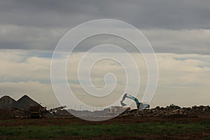 Diggers and trucks working together on a large industrial work site moving large stones and rubble into a large crusher to make