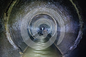 Diggers urban explorers are exploring underground river flowing in round sewer tunnel