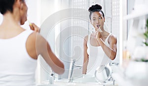 Digging deep to brush out all the cavities. an attractive young woman brushing her teeth while looking at the bathroom