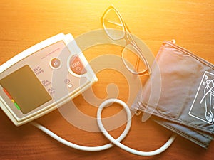 Digital blood pressure gauge and glasses are on the brown background