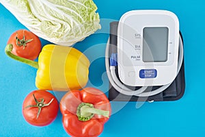 Digital blood pressure monitor and fresh vegetables on a blue background. Healthcare concept