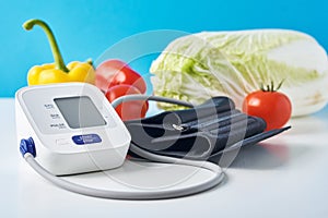 Digital blood pressure monitor and fresh vegetables on the table against blue background. Healthcare concept