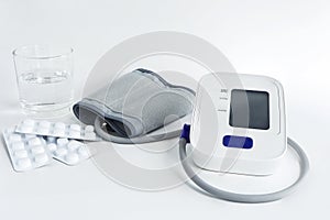 Digital blood pressure monitor and medicine pills on white background.