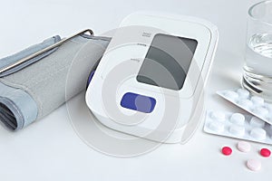 Digital blood pressure monitor and medicine pills on white background with copy space.
