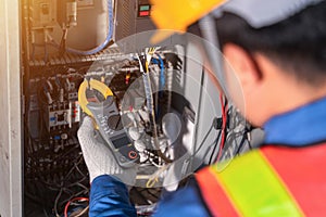 Digital clamp meter in hands of electrician close-up against background of electrical wires and relays. Adjustment of scheme of