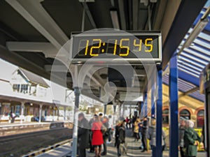 Digital clock marking 12:15:49, at a London train station