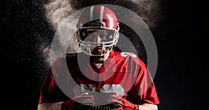 Digital composite of american football player holding ball against black background with smoke