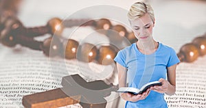 Digital composite image of caucasain young woman reading bible with rosary on book in background