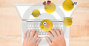 Digital composite image of emojis flying over hands using laptop at table