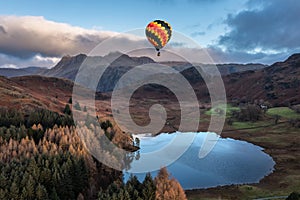 Digital composite image of hot air balloons over Beautiful landscape image of sunrise from Blea Tarn in Lake District during