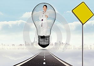 Digital composite image of smiling businesswoman in light bulb over road by signboard