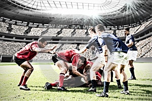 Digital composite image of team of rugby players tackling each other to win the ball in sports stadi