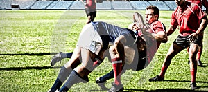 Digital composite image of team of rugby players tackling each other to win the ball in stadium