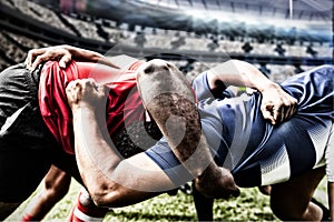 Digital composite image of two rugby players tackling each other in sports stadium