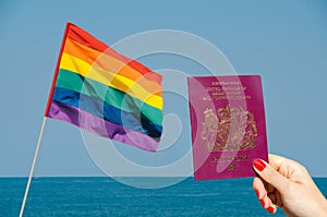 Digital composite of LGBT flag isolated overlooking the ocean with hand holding UK passport