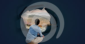 Man looking through surreal paper hole at nature landscape