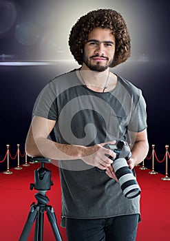 photographer rest on tripod, with the camera on hands in the red carpet. Flares behind photo