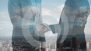 Digital composition of mid section of two businessmen shaking hands against aerial view of cityscape