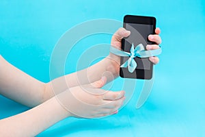 Digital detox concept. A children`s hand with a smartphone is tied with a blue ribbon and a second hand reaches for them.