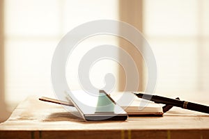 Digital Devices on Wooden Table, Blurred windows background, Smartphone with Note Book and Pen